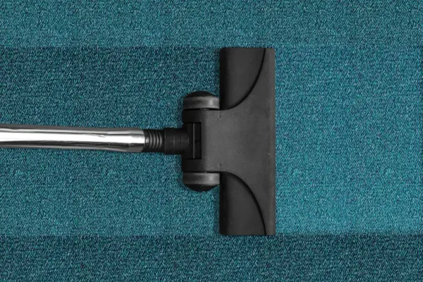Vacuum cleaner head sitting on teal carpet, leaving a clean track behind it