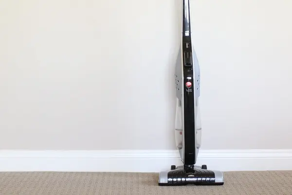 Clean lightweight stick vacuum standing upright on beige carpet against a wall